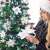 Woman decorating a Springos 120 cm diamond fir artificial Christmas tree with white decorations