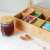 Navaris bamboo tea box with 10 compartments and glass lid, filled with tea bags, on a table with a cup of tea