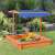 Child playing in the Timeless Tools wooden sandbox with blue canopy