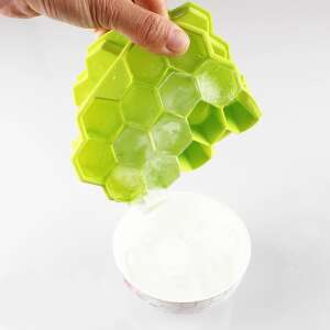 Green silicone ice cube tray with hexagonal molds, filled with ice cubes, being poured into a bowl - Ice cube tray
