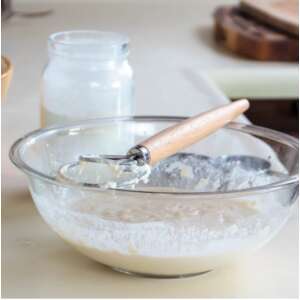 Stainless steel dough whisk with wooden handle in use, mixing dough in a glass bowl - Hand whisk