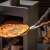 Pizza lapát fa nyéllel, amint egy pizzát vesznek ki egy kemencéből
