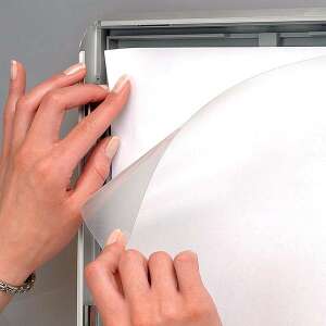 Kezek egy plakátot helyeznek be egy Opti Frame alumínium pattintós plakátkeretbe, a tiszta védőfólia látható - MT Displays