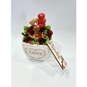Kerámia kaspó, benne egy mackó, aki piros szívet tart, piros virágokkal és mohával díszítve, a kaspón a LOVE felirattal - Ajándék ötlet Valentin-napra