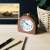 Navaris analog wooden alarm clock on a desk with a pen, pencil, and plant