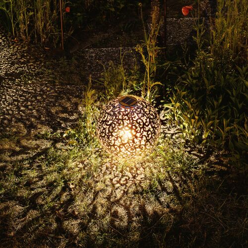 Oświetlona solarna latarnia Navaris rzucająca dekoracyjne cienie w ogrodzie