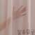Közelkép a halvány rózsaszín átlátszó függönyről, a szövet textúráját és a gondozási utasításokat mutatja
