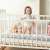 Ricokids gray braided crib bumper, installed in a crib, with a child standing next to it