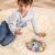 Young child playing with Viga PolarB wooden shape sorting clock on a rug.