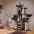 Black cat tree with scratching posts, multiple platforms, hanging toys, and a hammock in a living room setting