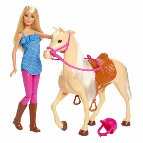 Barbie baba kék felsőben, rózsaszín nadrágban és barna csizmában, egy világosbarna ló mellett áll rózsaszín kantárral, barna nyereggel és egy rózsaszín lovagló sisakkal a földön, fehér háttéren. - Barbie