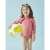 Little girl wearing Archimedes UV protective swimsuit set, 18-24 months, pink with gold firework print, holding a beach ball