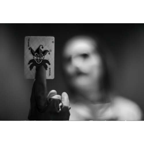 Fekete-fehér fotó egy kézről, amely egy Joker kártyát tart 