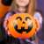 Găleată de Halloween în formă de dovleac cu bomboane, dovleac din plastic portocaliu cu față neagră, mâner, ținută de o fată în costum de vrăjitoare