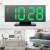 Green LED digital alarm clock with mirror display, showing time, alarm, and PM indicator, on a table with other objects in the background