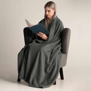 Woman wrapped in DecoKing Henry graphite grey embossed blanket reading a book - Interior design