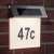 Solar powered house number sign with LED lights, stainless steel, 47C, mounted on brick wall