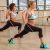 Két nő kitörés gyakorlatot végez Pilates rúddal és ellenállás szalagokkal