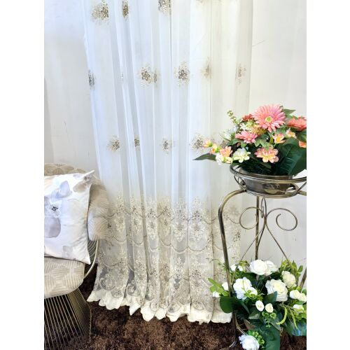 Elegáns, áttetsző függöny virágmintás hímzéssel, ekrü, barna és arany színekben, nappali környezetben.