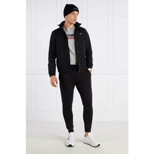 Tommy Hilfiger Herren schwarze Jacke, Ganzkörperansicht, Modell trägt die Jacke mit schwarzer Hose und weißen Sneakern