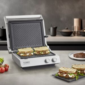 Електрически контактен грил Caso Germany SteakChef 2 в 1 с отворен капак, показващ гриловани сандвичи и пържола, идеален за приготвяне на различни ястия, антиприлепващо керамично покритие, лесно почистване - Барбекю на маса