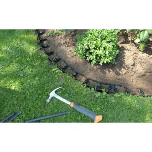 Fekete műanyag ágyásszegély telepítve egy kertben, kalapáccsal és extra darabokkal - Ágyásszegély