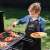 Child wearing a black grill apron with red trim, grilling food on a barbecue