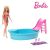 Barbie baba áll egy kék medence mellett rózsaszín csúszdával és létrával, két rózsaszín és lila pohár és egy törölköző van a szélén