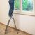 Woman standing on foldable steel step ladder cleaning window