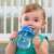 Baby drinking from Chicco Training Cup 2in1, blue dinosaur design, with removable spout
