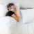 Nő alszik az ágyban Medi Sleep rózsaszín 3D alvómaszkot viselve