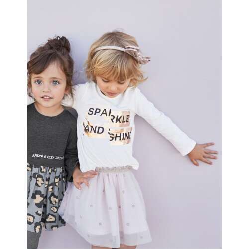 Dziewczynka w białej koszulce z długim rękawem z nadrukiem 'Sparkle and Shine' i różową spódnicą tiulową