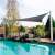 Grey triangular sunshade installed over a swimming pool, providing shade from the sun