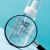 Purles 142 Perfector Concentrate csepegtetős flakon nagyítón keresztül nézve kék háttér előtt, kiemelve a termék részleteit és a márka információit