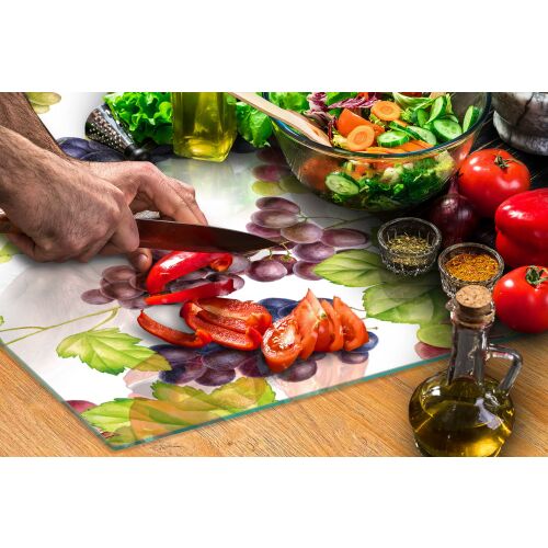 Személy az ÜVEG VÁGÓDESZKA 52x30 GYÜMÖLCS üveg vágódeszkát használja szőlő mintával pirospaprika és paradicsom aprításához, friss alapanyagokkal és olívaolajjal körülvéve, konyhai környezetben - Vágódeszka