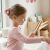 Egy fiatal lány világosbarna hajjal, egy nagy Hello Kitty rózsaszín csillámos hajcsattal a hajában, mosolyogva néz a tükörbe, bemutatva a terméket használat közben otthoni környezetben
