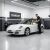 Szerelő vizsgál egy fehér Porsche 911 Carrera 4 Cabriolet 997.1-et egy professzionális garázsban TeamCar márkajelzéssel, utalva a szakértő gondozásra és a termék integrációjára