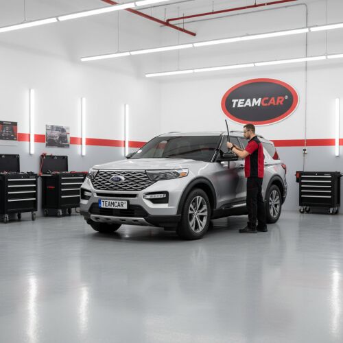 Férfi TeamCar ablaktörlő lapátokat szerel egy Ford Explorer Gen VI U6 SUV-ra egy garázsban, bemutatva a termék használatát 
