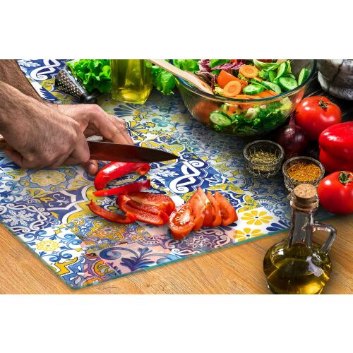 Személy pirospaprikát vág egy ÜVEG VÁGÓDESZKA 52x30 MOZAIK üveg vágódeszkán mozaik mintával, konyhai környezetben salátával és fűszerekkel - Vágódeszka