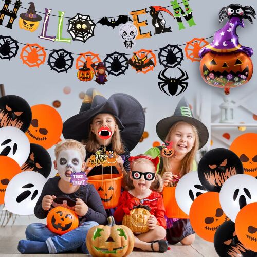 Halloween jelmezbe öltözött gyerekek Halloween témájú kellékeket tartva, szellem, tök és fekete latex lufikkal körülvéve, 'Happy Halloween' transzparenssel és fólia lufival a háttérben, vidám Halloween parti hangulatot ábrázolva - Halloweeni dekoráció
