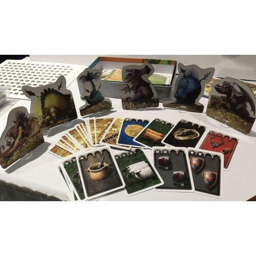 Dragons társasjáték alkatrészek, beleértve sárkányfigurákat, kártyákat juhokkal, arannyal és bájitalokkal, fehér felületen elrendezve, játékra készen - Matagot
