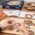 Személy szereli össze a ROKR 3D Zodiákus fa falióra puzzle-t, látszanak a fa alkatrészek, az útmutató és a csomagoló doboz