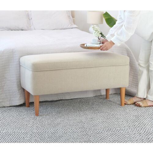 Atelier Del Sofa Pouffe Cream Glend az ágy végén elhelyezve egy világos és tágas hálószobában, egy személy egy tálcával a tetején interakcióba lép, kiemelve a sokoldalúságát - Lábtartó és puff