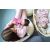 Nő gyengéden cumisüvegből eteti a csecsemőt, mellette egy másik baba alszik egy bölcsőben, mindannyian Moniel Basic Powder pink melegítőben, hangsúlyozva a családi melegséget és kényelmet