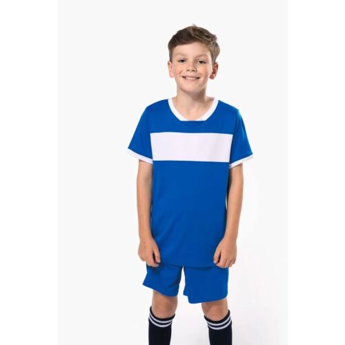 Mosolygó kisfiú viseli a kék-fehér Proact PA4001 GYERMEK RÖVIDUJJÚ JERSEY PÓLÓ rövid ujjú jersey pólót és hozzá illő rövidnadrágot, focira vagy sportolásra alkalmas - Gyerek focimez