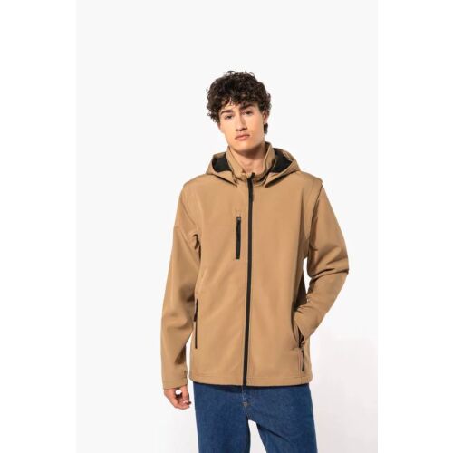 Fiatal férfi visel világosbarna Kariban KA422 uniszex 3 rétegű softshell kapucnis kabátot levehető ujjakkal és kék farmert, stúdióban áll fehér háttérrel, bemutatva a kabát illeszkedését és elülső részleteit. - Férfi kabát