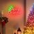 Elegáns „Merry Christmas” neonfelirat zöld karácsonyfával és piros szöveggel, kandalló fölött elhelyezve, ünnepi zoknikkal és dekoratív rénszarvassal, megvilágított karácsonyfa mellett, otthonos beltéri ünnepi környezetben.