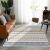 Conceptum Hypnose szőnyeg 180x280 Többszínű W1079 egy modern nappali környezetben barna kanapéval, székkel és nagy ablakkal, kiemelve élénk és változatos geometrikus mintázatait