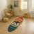 Conceptum Hypnose szőnyeg (100 x 300) Többszínű 292, ovális, szörfdeszka alakú szőnyeg 'California Surfing' mintával, naplementében szörfös sziluettje és pálmafák láthatók, világos nappaliban, rattan bútorok és növény mellett, hangulatos és pihentető dekorációt mutat be.