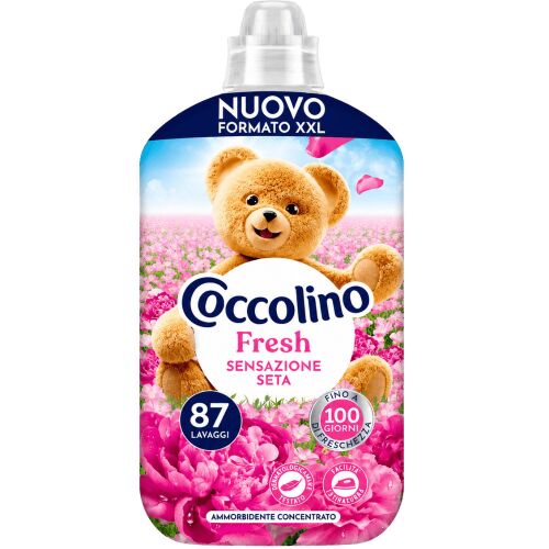 Coccolino Fresh Sensazione Seta öblítő koncentrátum, 1,827 L-es flakon, 87 mosáshoz elegendő, selymes és gyümölcsös virágillattal. Az XXL formátumú csomagoláson a Coccolino mackó rózsaszín virágok között látható. - Öblítő